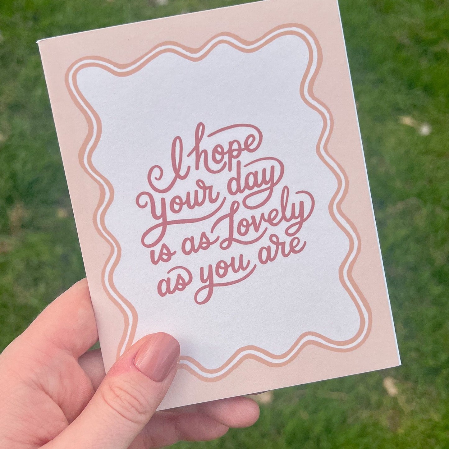 Pink Lovely Day greeting card being held over grass