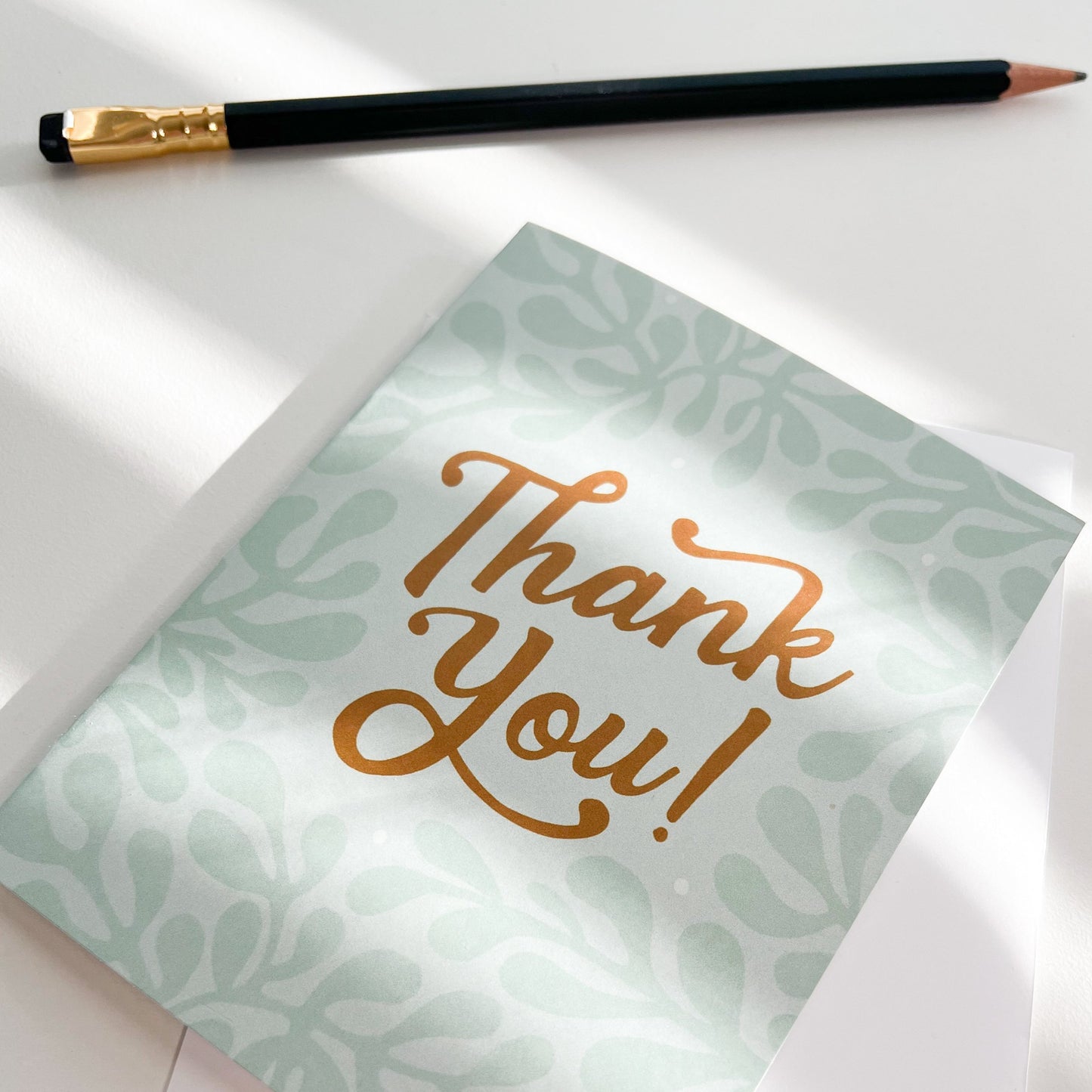 Thank You Card with white envelope shown on white desk with pencil and sunlight rays coming through window.