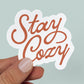 Sticker with quite "stay cozy" in red script lettering