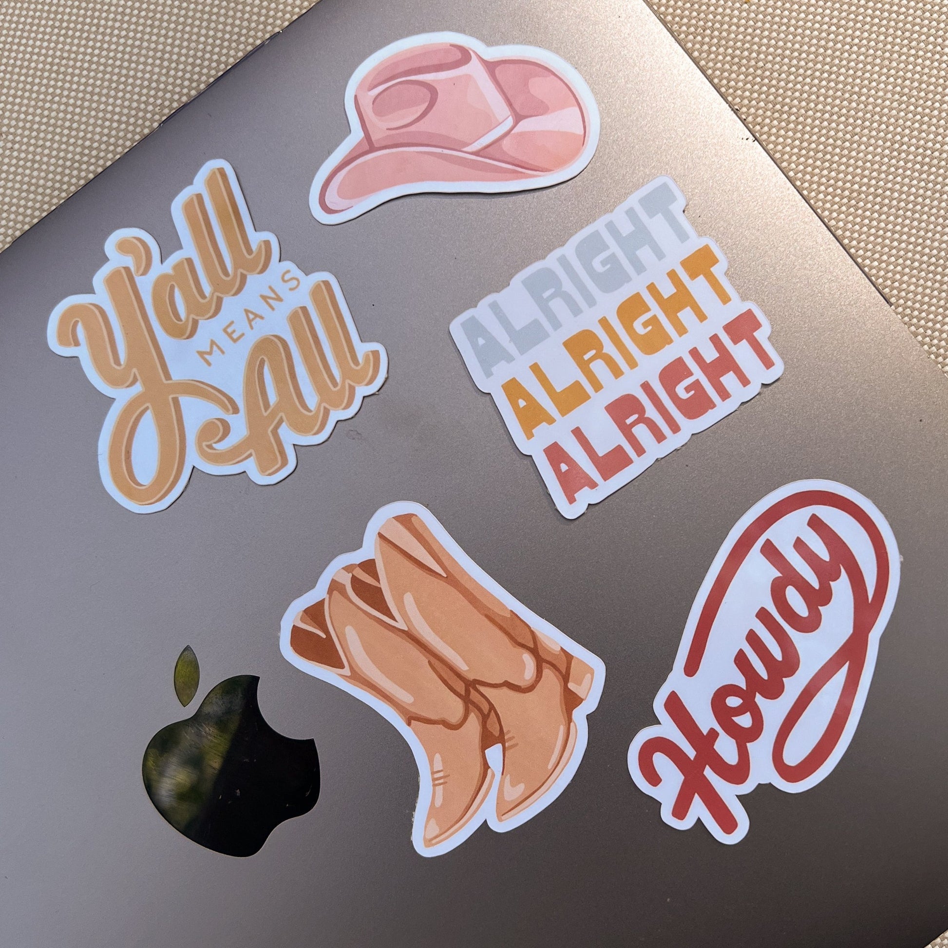 5 Funky Cowboy Stickers, including the Alright Alright Alright Sticker, on the front of a Macbook Pro.