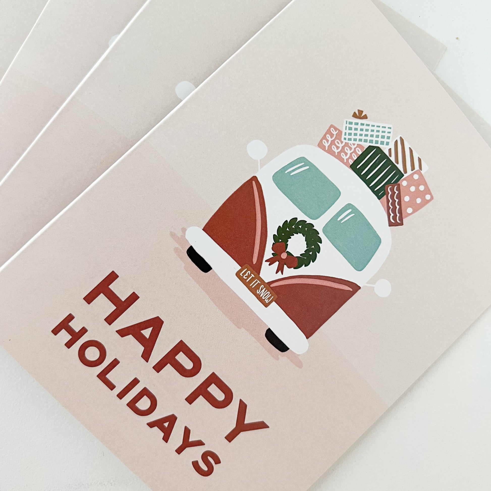 Stack of pink cards depicting a vintage-style van with presents on top and the message "Happy Holidays"