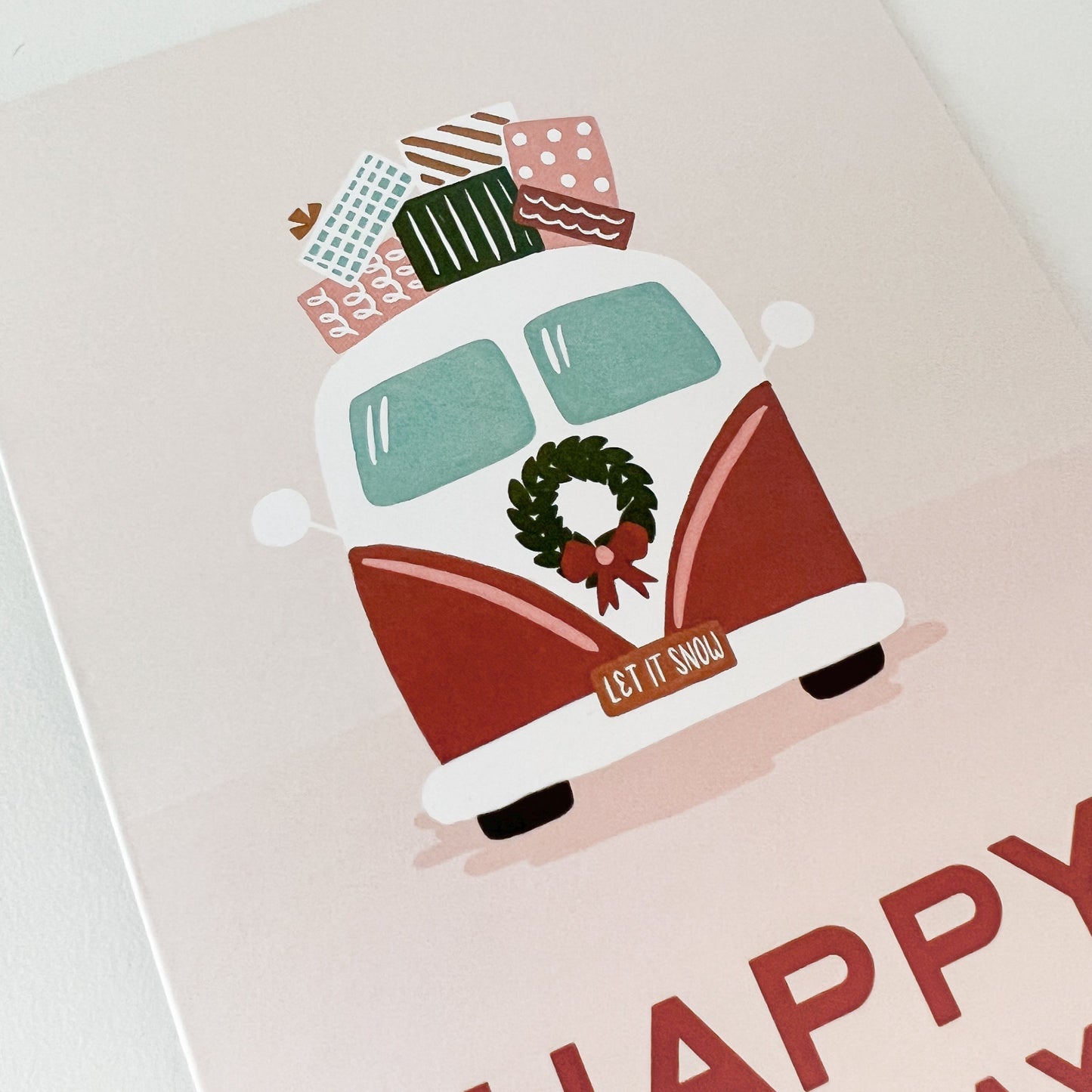 Close-up of pink card depicting a vintage-style van with presents on top and the message "Happy Holidays"