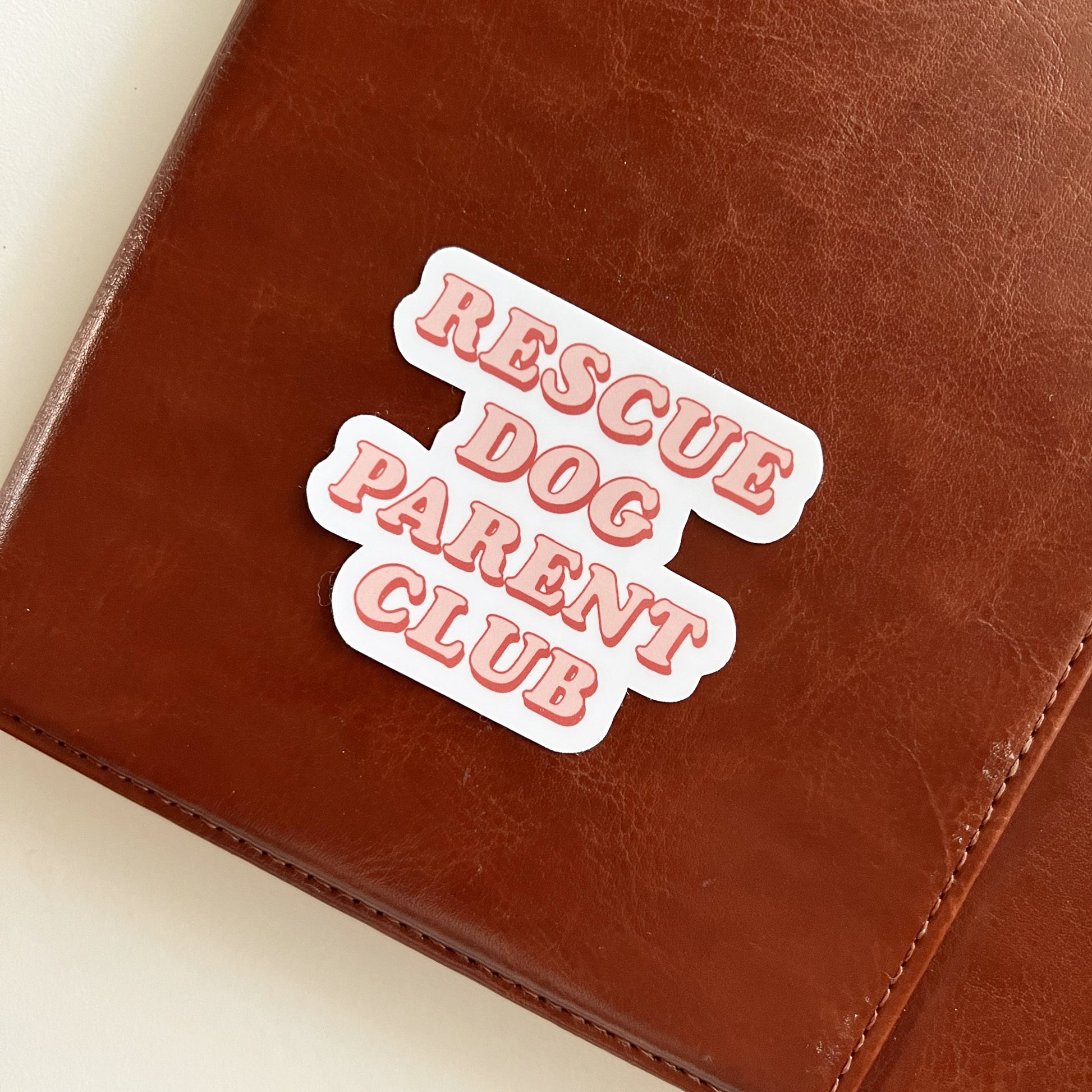 Rescue Dog Parent Club Sticker shown on brown journal..