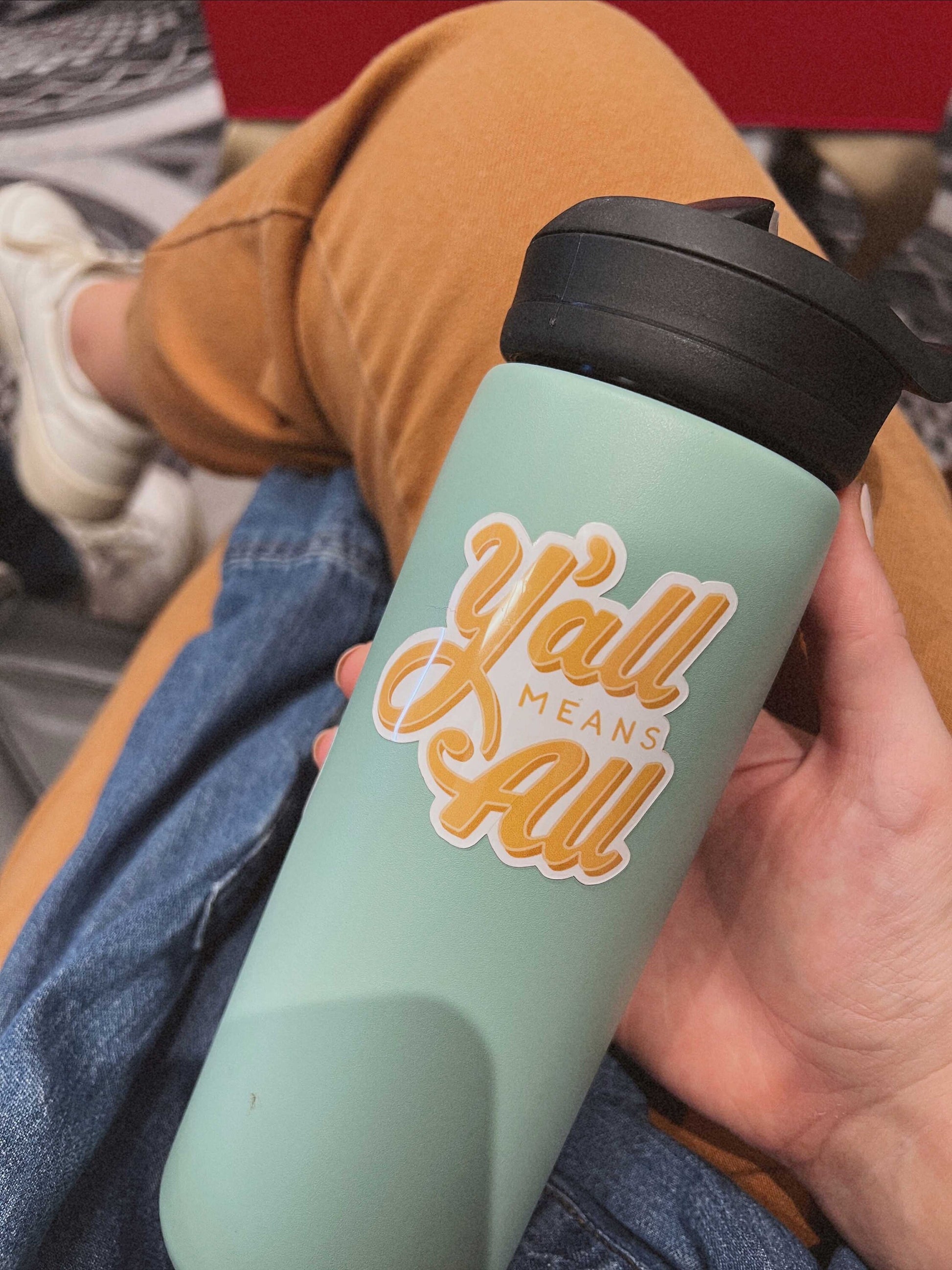 Yellow "Y'all Means All" Sticker on water bottle.